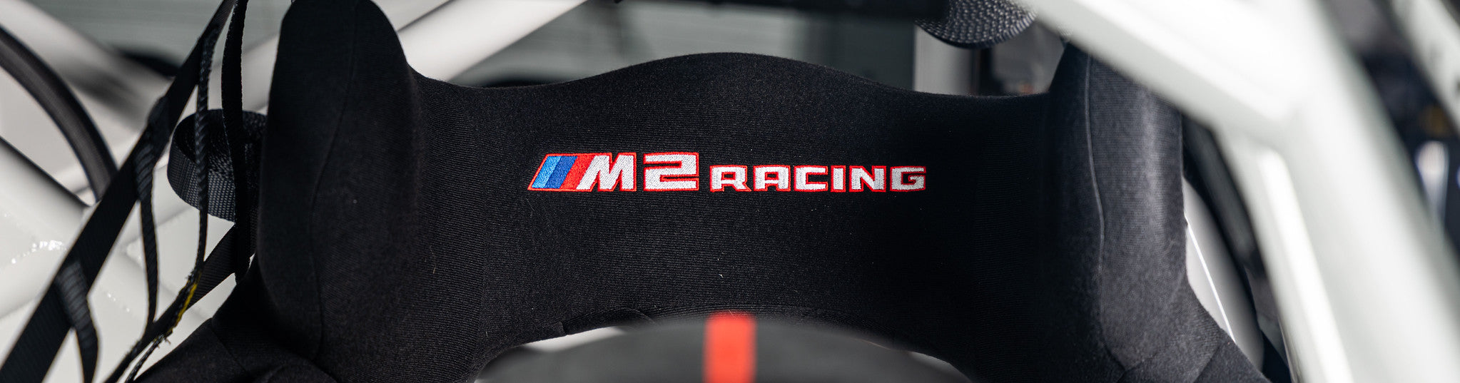 Close-up of the BMW M2 Racing Sabelt racing seat headrest featuring the embroidered M2 Racing logo within the motorsport cockpit.