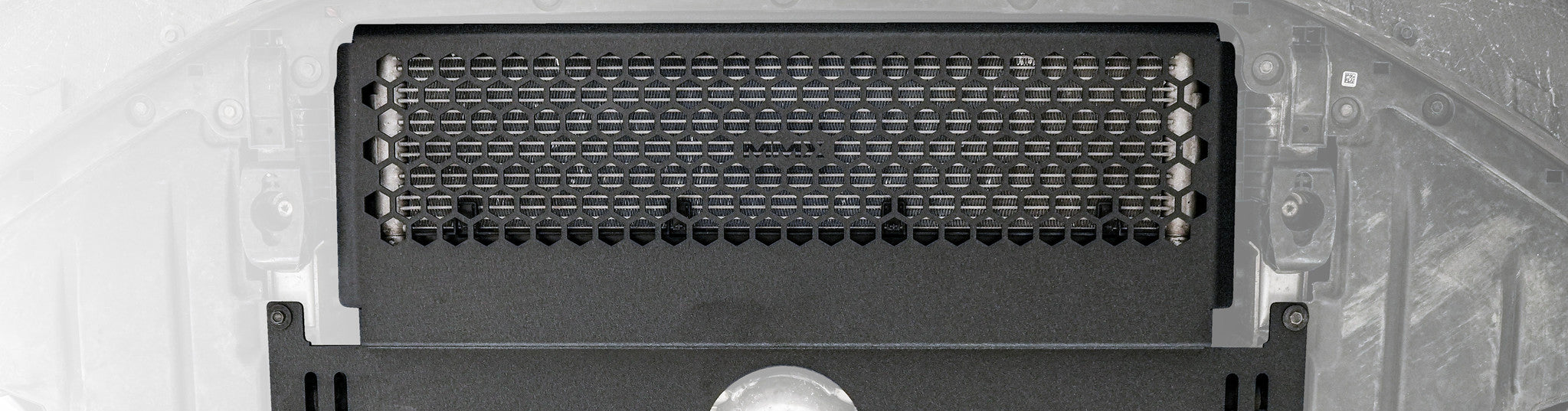 Close-up of the MMX Performance Oil Cooler Guard installed beneath a BMW G87 M2, showcasing the precision-formed 6061-T6 aluminum construction and optimized hexagonal grille protecting the factory S58 oil cooler.