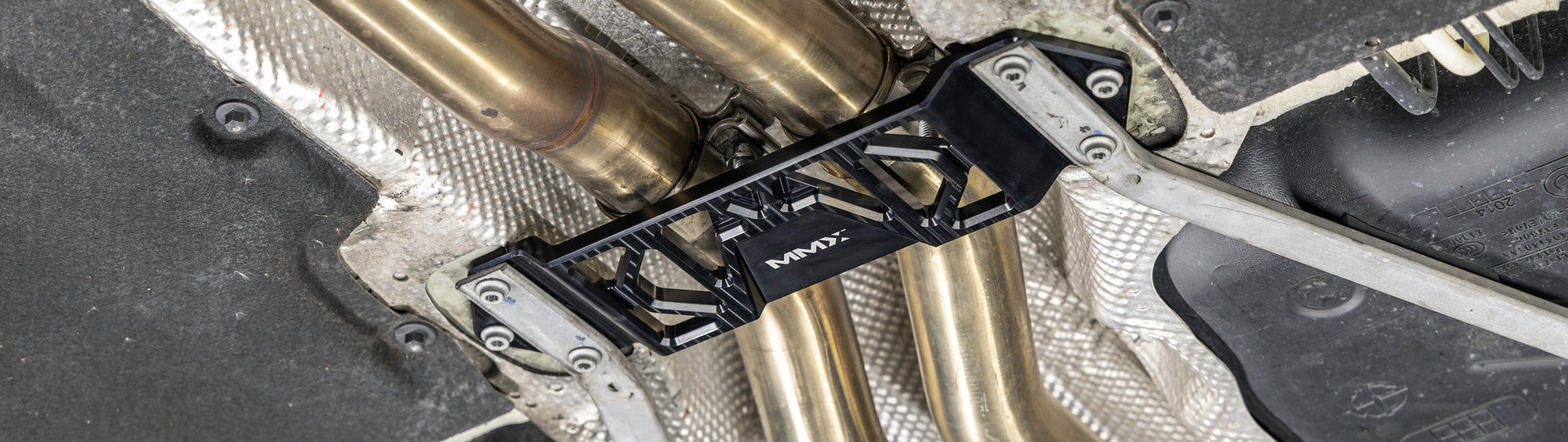 MMX Performance Underbody Chassis Brace installed on a BMW M car, providing increased exhaust clearance and improved chassis rigidity