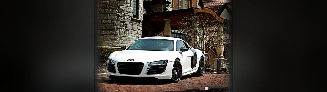 White Audi R8 with black wheels parked on a brick driveway in front of a stone Tudor-style mansion