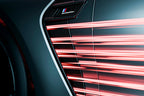Close-up of a car's air vent with red light streaks, featuring a brand logo.