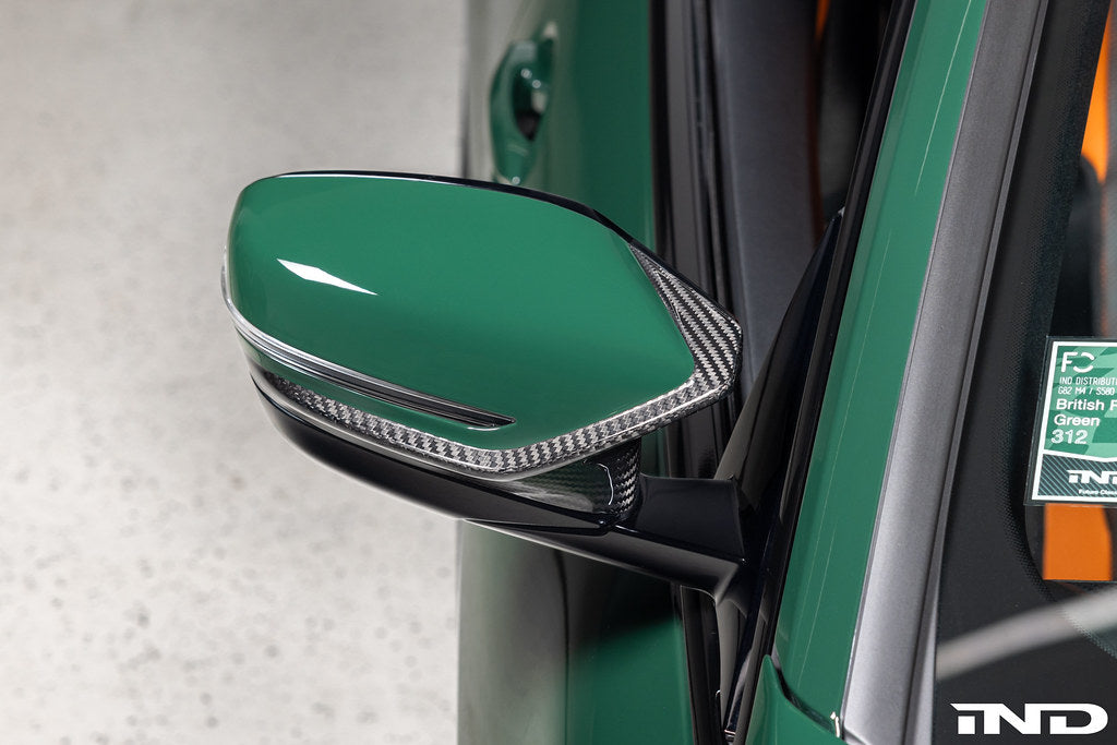 Alpha N G8X M2/M3/M4 carbon mirror cap set on exterior car side, showcasing sleek black finish and aerodynamic design.
