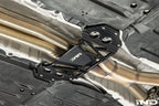 MMX Performance billet aluminum underbody chassis brace installed on a BMW G8X M3 and M4, providing an additional 15mm of exhaust clearance while increasing chassis rigidity for aftermarket exhaust systems.