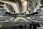 MMX Performance billet aluminum underbody chassis brace installed on a BMW G8X M3 and M4, providing an additional 15mm of exhaust clearance while increasing chassis rigidity for aftermarket exhaust systems.