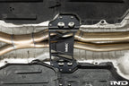 MMX Performance billet aluminum underbody chassis brace installed on a BMW G8X M3 and M4, providing an additional 15mm of exhaust clearance while increasing chassis rigidity for aftermarket exhaust systems.