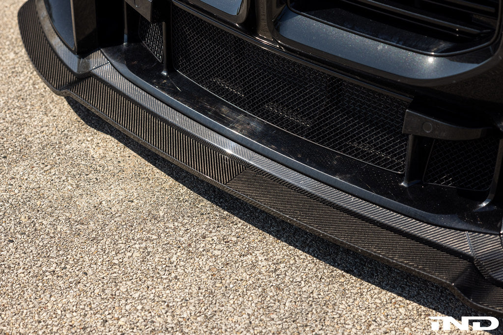Alpha N G87 M2 Carbon adjustable front lip installed on a vehicle, showcasing its sleek design and aerodynamic exterior enhancement.