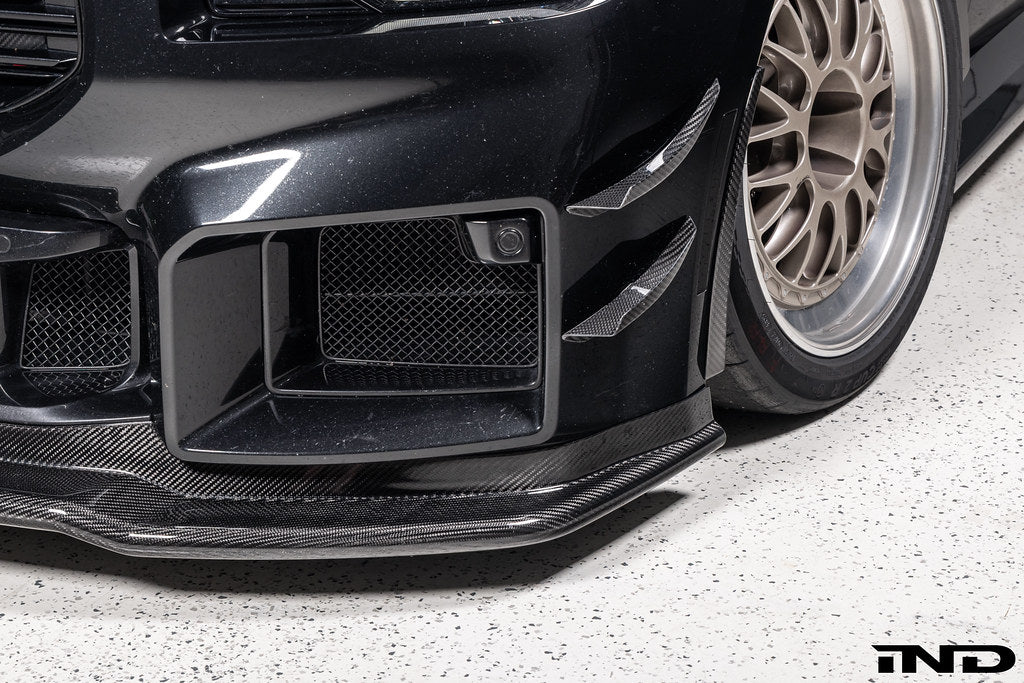 Alpha-N Carbon Corse front splitter installed on a Black Sapphire BMW G87 M2, enhancing the front-end appearance with pre-preg carbon fiber construction and aggressive styling.