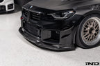 Alpha-N Carbon Corse front splitter installed on a Black Sapphire BMW G87 M2, enhancing the front-end appearance with pre-preg carbon fiber construction and aggressive styling.