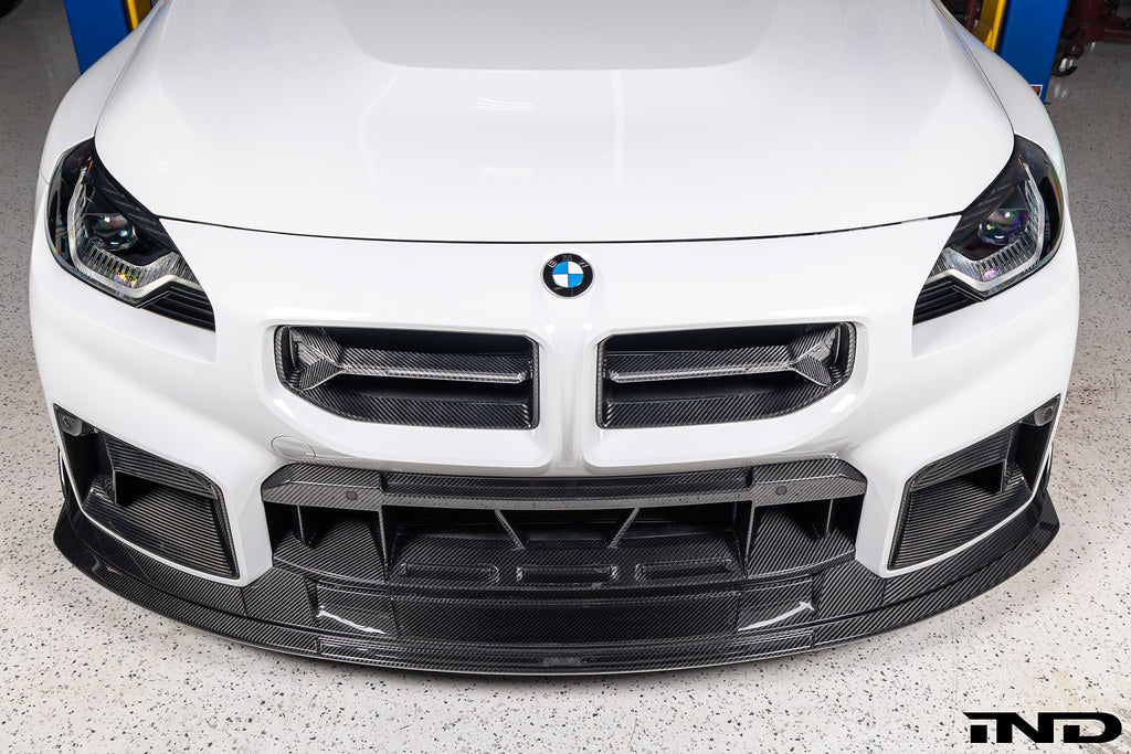 Alpha-N V2 Carbon Front Grille installed on an Alpine White BMW G87 M2, front view showcasing the aggressive motorsport-inspired design and exposed carbon fiber construction.