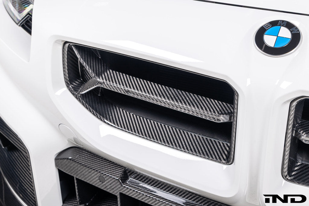 Alpha-N V2 Carbon Front Grille installed on an Alpine White BMW G87 M2, front view showcasing the aggressive motorsport-inspired design and exposed carbon fiber construction.