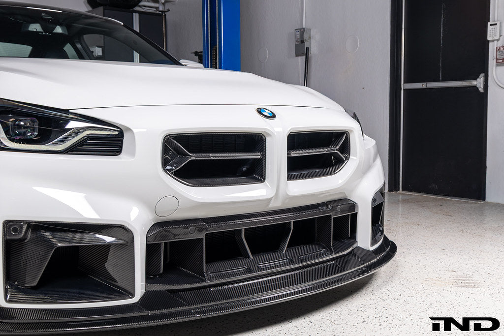 Alpha-N V2 Carbon Front Grille installed on an Alpine White BMW G87 M2, front view showcasing the aggressive motorsport-inspired design and exposed carbon fiber construction.