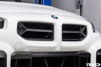 Alpha-N V2 Carbon Front Grille installed on an Alpine White BMW G87 M2, front view showcasing the aggressive motorsport-inspired design and exposed carbon fiber construction.