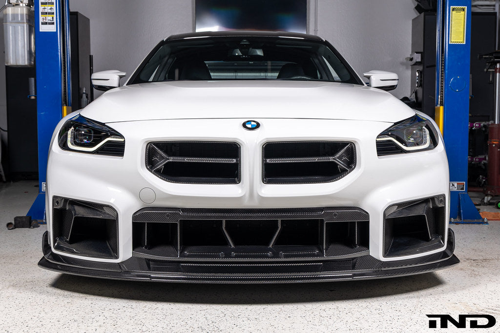 Alpha-N V2 Carbon Front Grille installed on an Alpine White BMW G87 M2, front view showcasing the aggressive motorsport-inspired design and exposed carbon fiber construction.