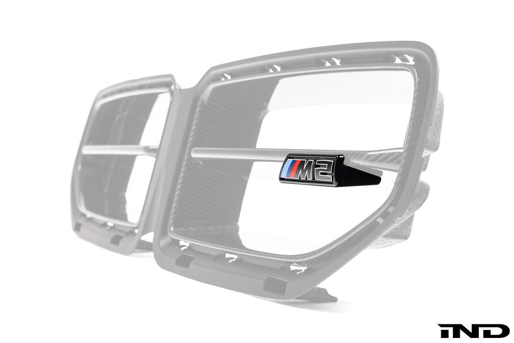 Alpha N G87 M2 LCI front grille emblem retainer with BMW OEM M2 badge installed on the vehicle exterior.