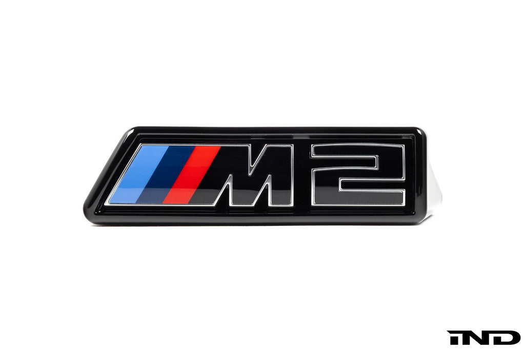 Alpha N G87 M2 LCI front grille emblem retainer with OEM M2 badge on white background, for BMW exterior customization.