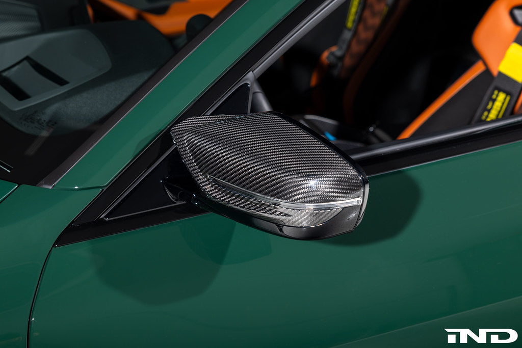 Alpha N G8X M2, M3, M4 carbon mirror cap set installed on exterior side of BMW vehicle, showcasing sleek black carbon finish.