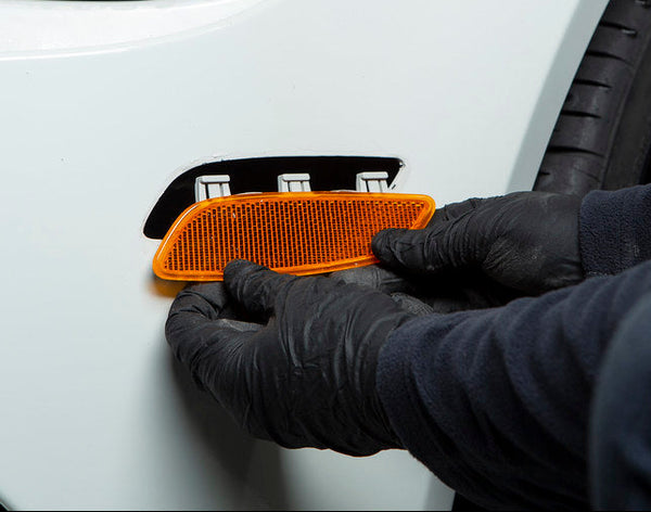 Factory amber front reflector being removed from the front bumper of an Alpine White BMW E90 M3 during installation of the IND Painted Front Reflector Set.