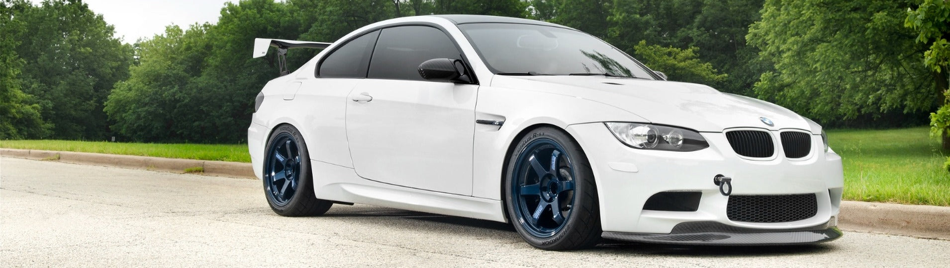 Alpine White BMW E92 M3 featuring IND Painted Front Reflectors, blue Volk TE37 wheels, and a tree-lined background, showcasing a clean European-inspired OEM+ front-end appearance.