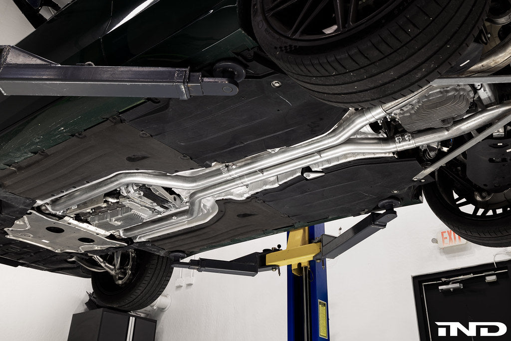 Eisenmann non-resonated center pipe set installed on a BMW F95 X5M and F96 X6M LCI mild hybrid while mounted on a vehicle lift, showing the complete exhaust installation