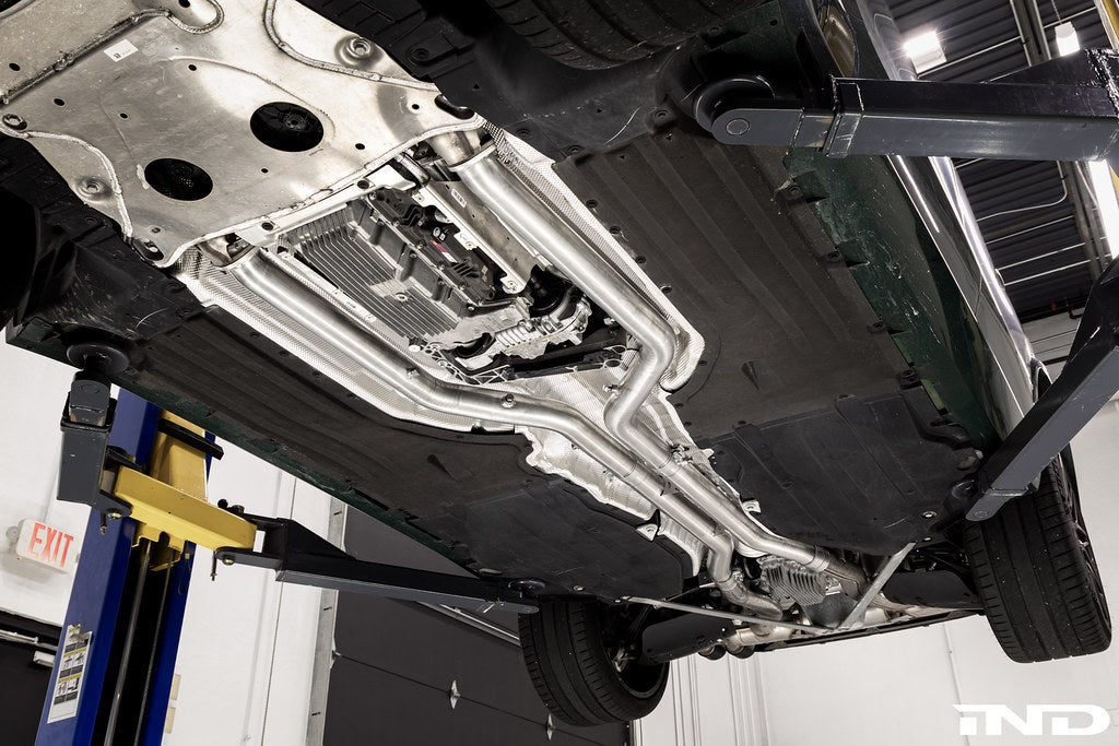 Eisenmann non-resonated center pipe set installed on a BMW F95 X5M and F96 X6M LCI mild hybrid while mounted on a vehicle lift, showing the complete exhaust installation