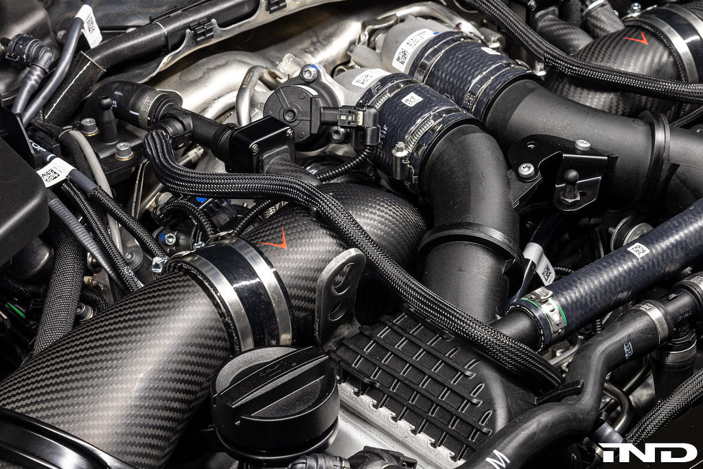Close-up of matte carbon turbo inlet set installed on BMW G90 G99 M5 (S68) by Eventuri, showcasing high-performance engine components.