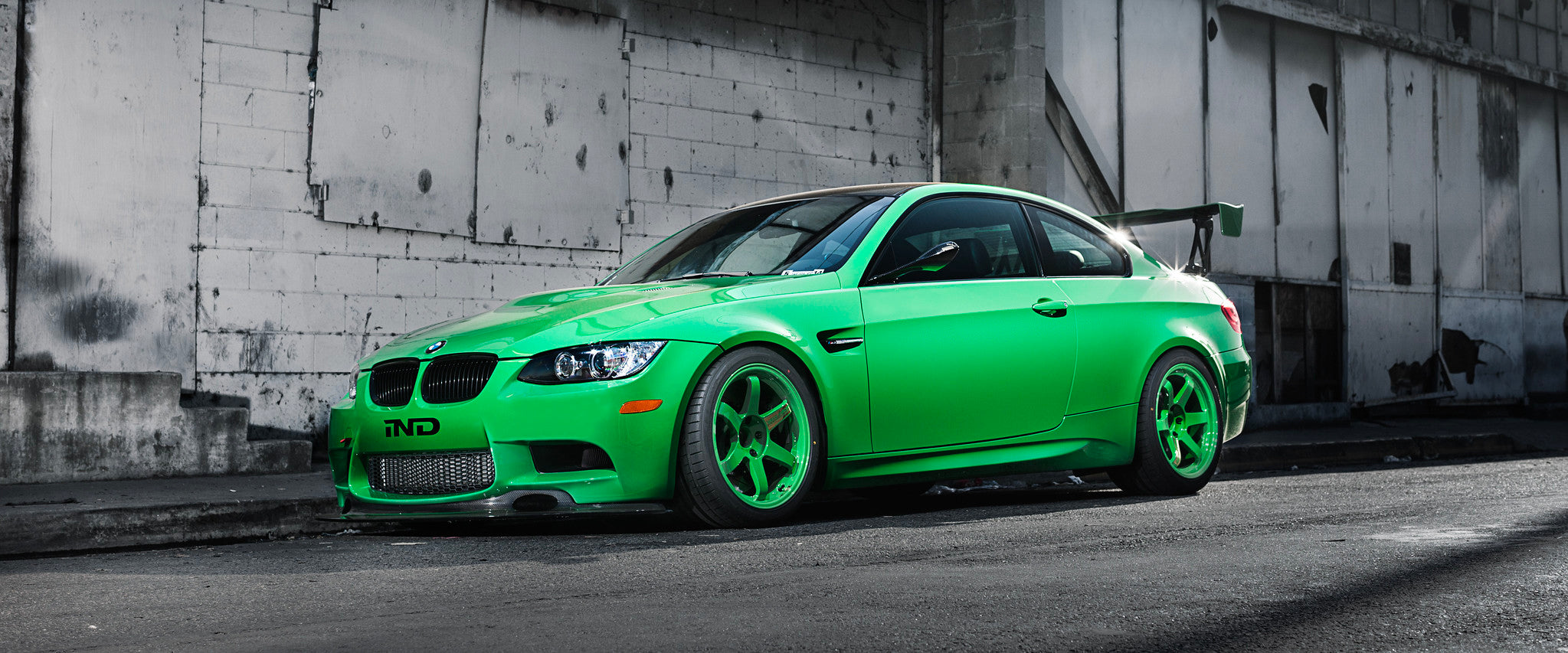 Front driver-side angle view of an IND BMW E92 M3 finished in Signal Green with green Volk TE37 wheels and a Varis Japan rear wing, featured as a homepage hero image.