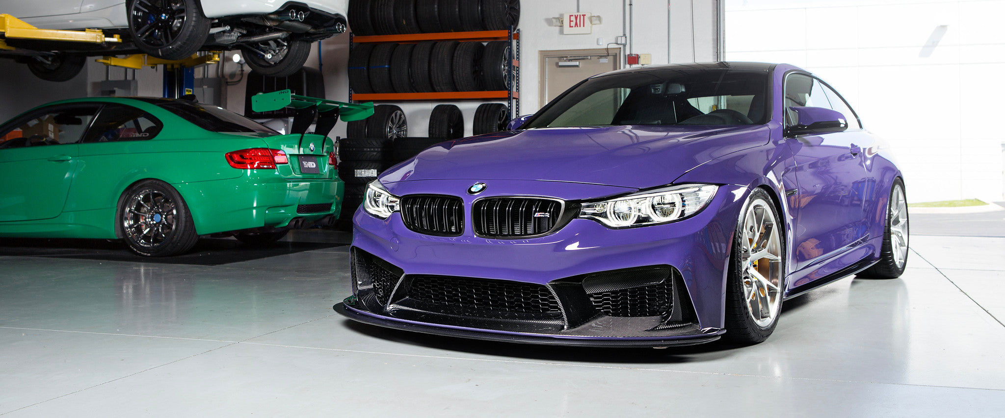 Front view of IND's BMW F82 M4 finished in Ultraviolet Purple with a 3D Design front bumper, photographed inside the IND Distribution warehouse as a homepage hero image.