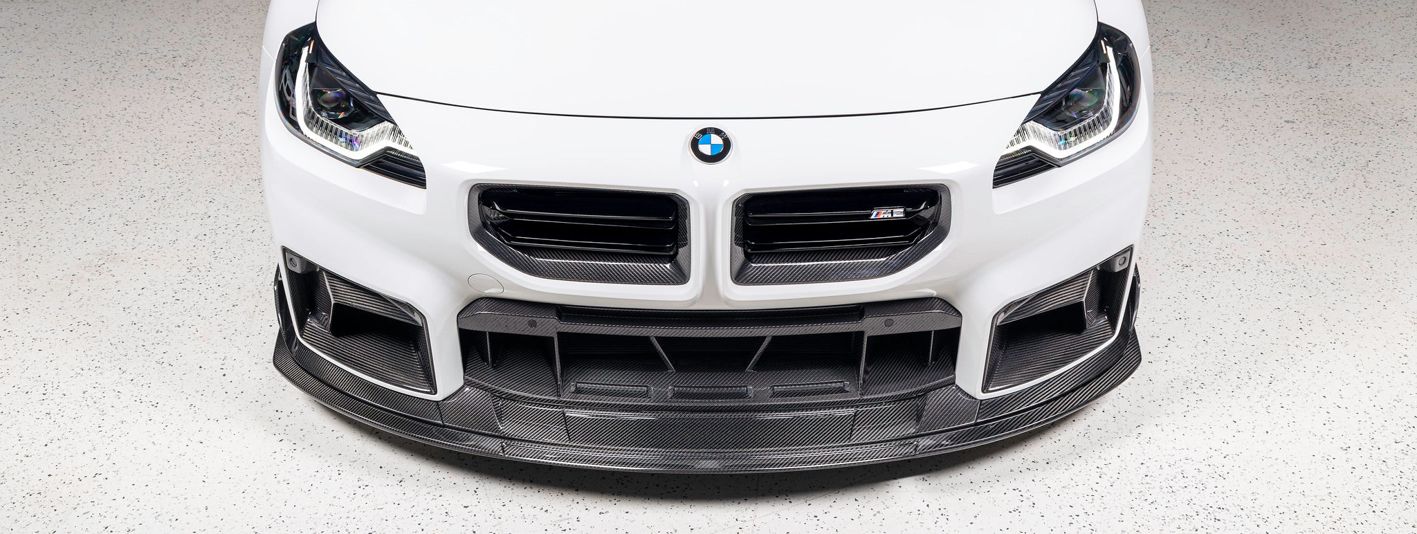 TREVORA TR87 Track pre-preg carbon fibre front splitter installed on Alpine White BMW G87 M2 front view showcasing the aggressive twin-level splitter design