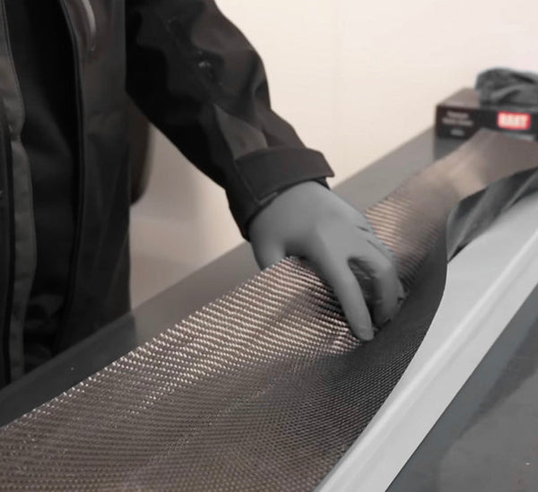 Close-up of a TREVORA technician applying pre-preg carbon fiber material to a mold for composite component production
