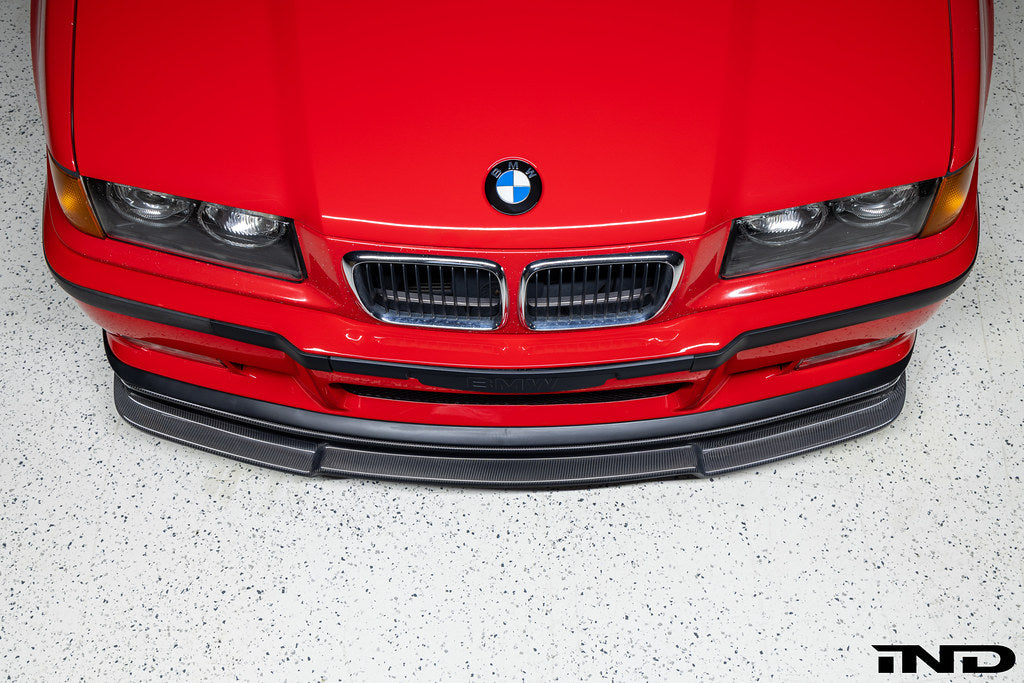 Alpha N E36 M3 Carbon GT front lip installed on red BMW E36 M3, showcasing sleek exterior automotive styling.