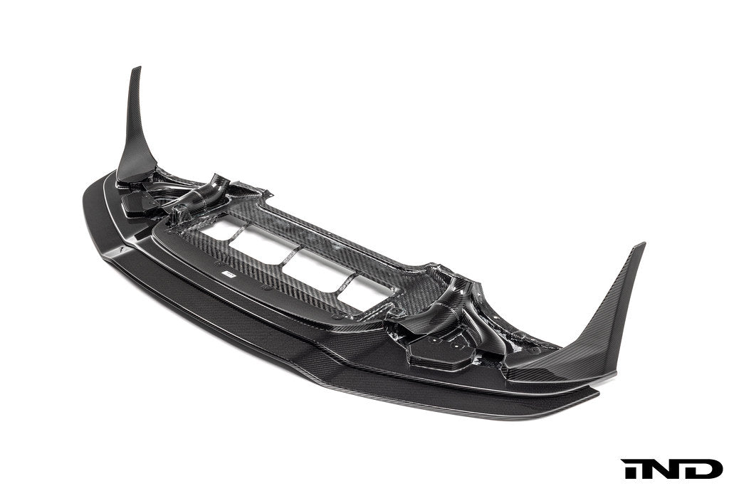 Alpha N F87 M2 Competition CS Carbon Corse front splitter mounted on a white background, showcasing its aerodynamic design and carbon fiber finish.