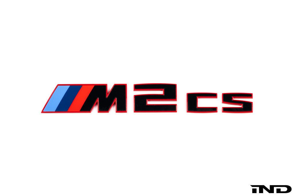 BMW G87 M2 CS trunk emblem in gloss black with red border on a white background, exterior car badge detail.