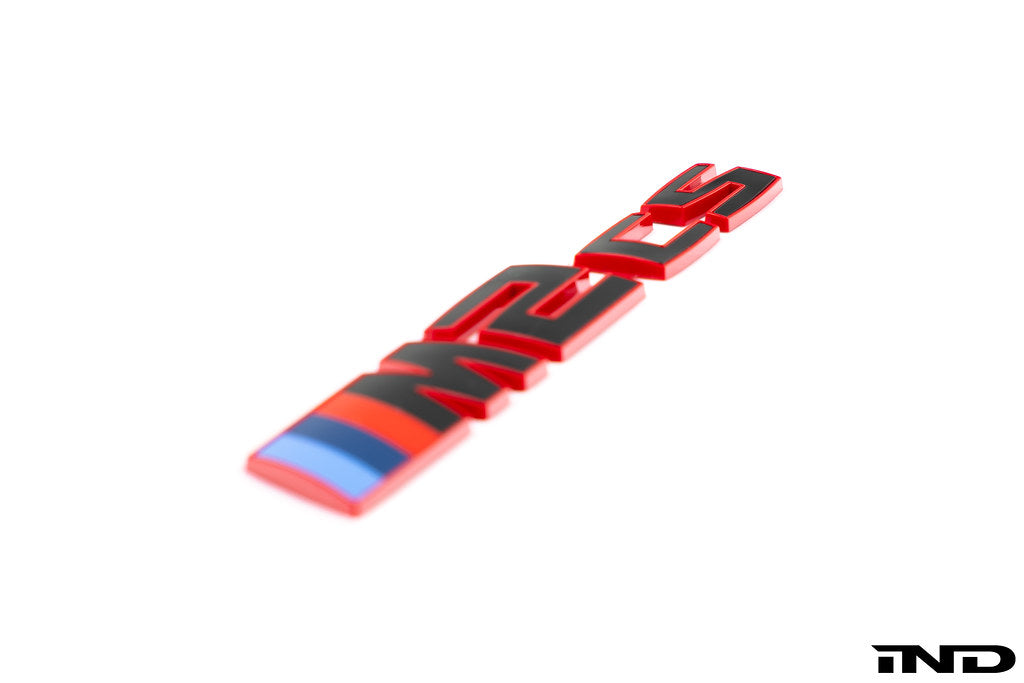 BMW G87 M2 CS trunk emblem in gloss black with red border on a white background, exterior car accessory.