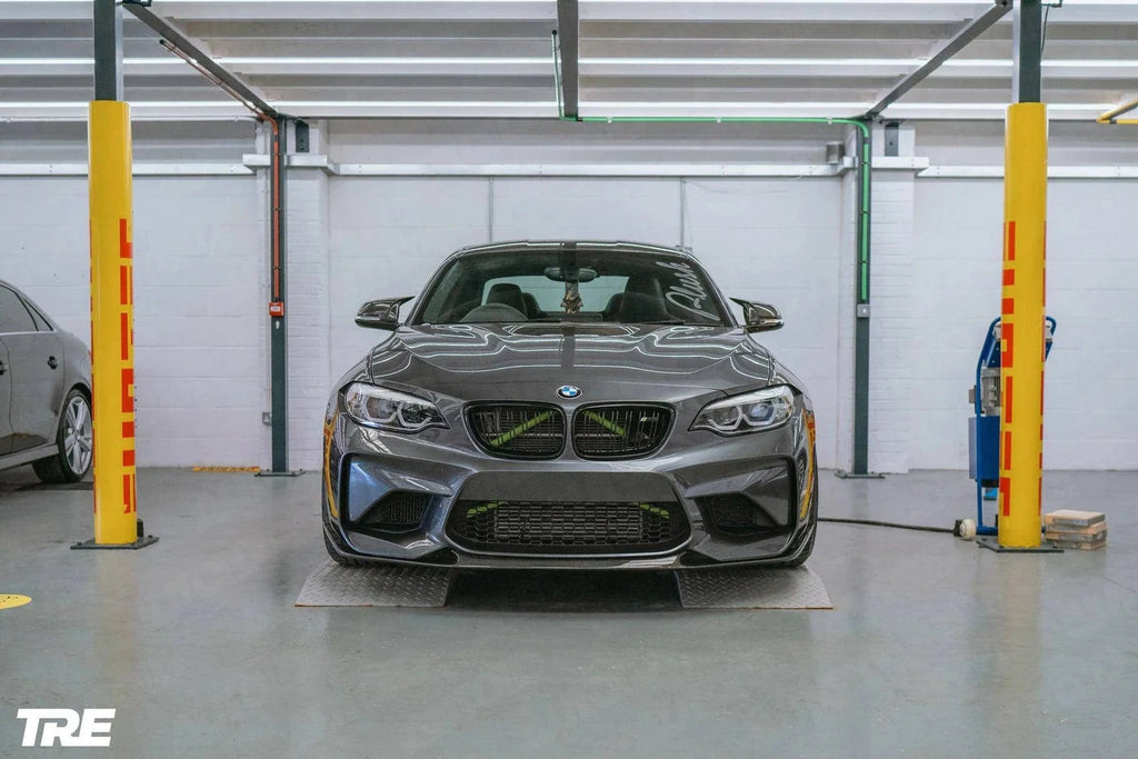 TREVORA BMW F87 M2 OG Pre-Preg Carbon Front Splitter, exterior view showing sleek carbon fiber design on car's front bumper.