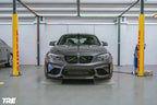 TREVORA BMW F87 M2 OG Pre-Preg Carbon Front Splitter, exterior view showing sleek carbon fiber design on car's front bumper.