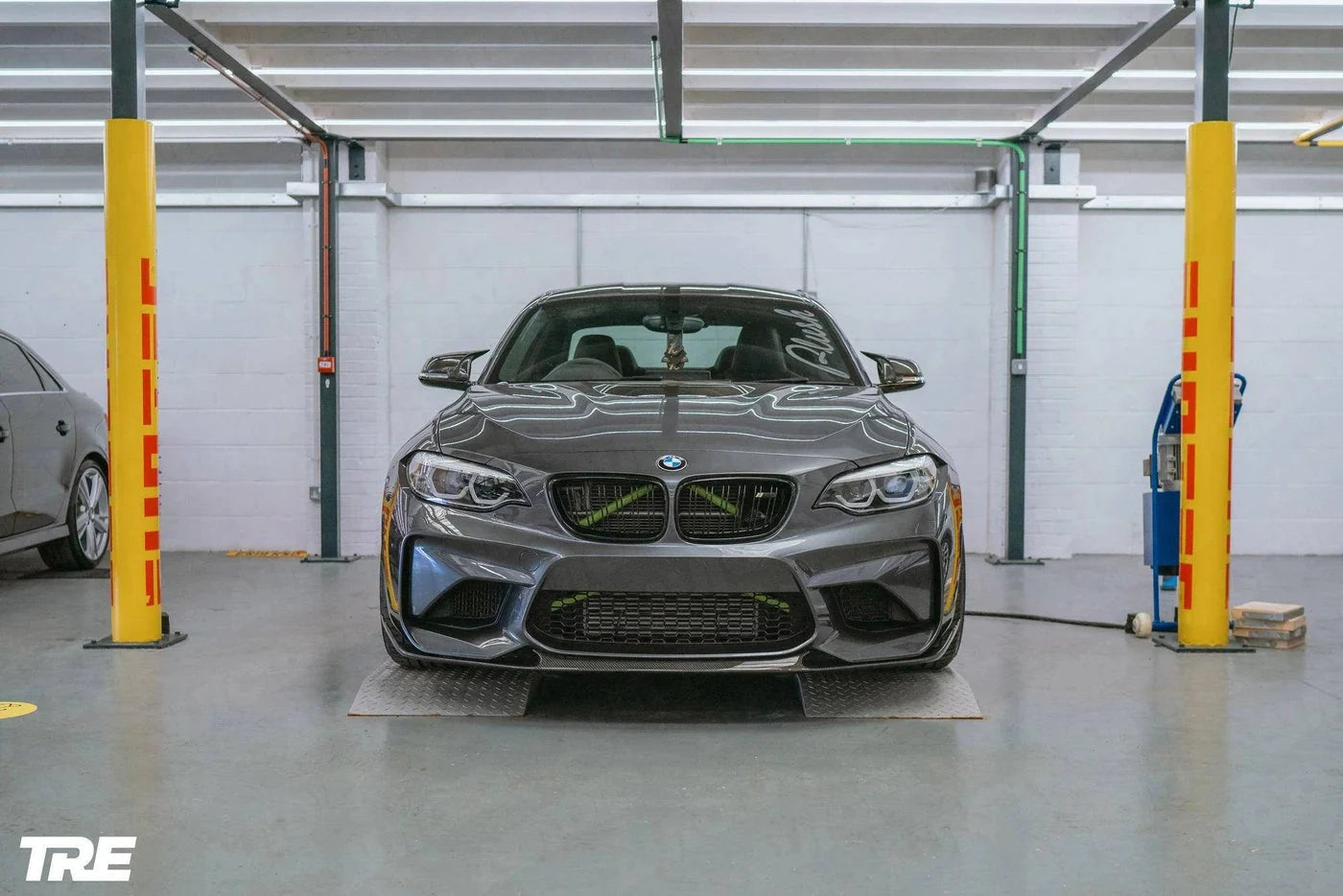 TREVORA BMW F87 M2 OG Pre-Preg Carbon Front Splitter, exterior view showing sleek carbon fiber design on car's front bumper.