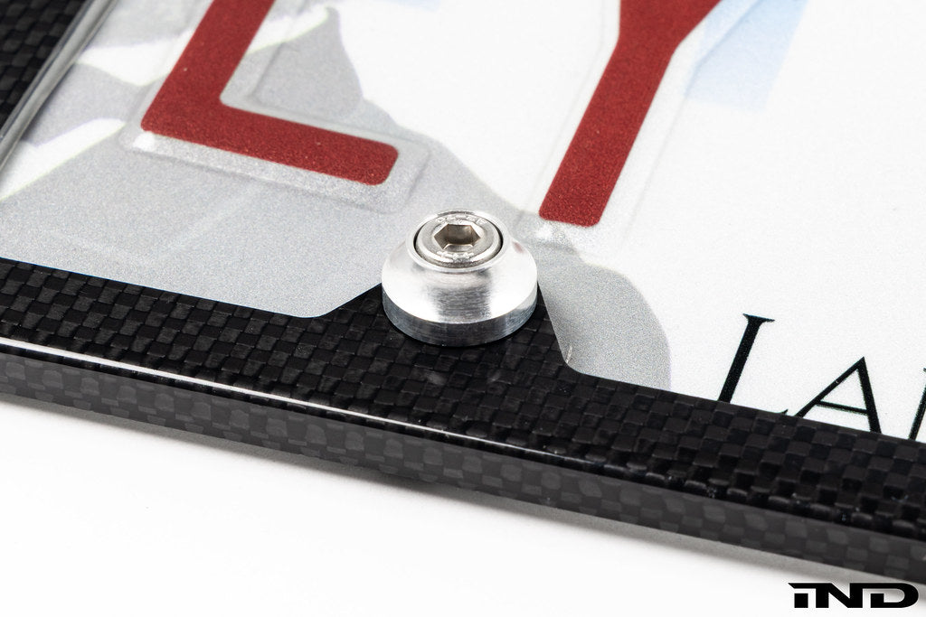 Downstar BMW License Plate Dress Up Hardware installed on a license plate with a carbon fiber license plate frame, featuring stainless steel fasteners and billet aluminum beauty washers, shown on a white background.