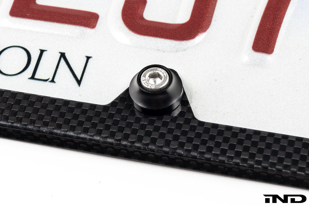 Downstar BMW License Plate Dress Up Hardware installed on a license plate with a carbon fiber license plate frame, featuring stainless steel fasteners and billet aluminum beauty washers, shown on a white background.