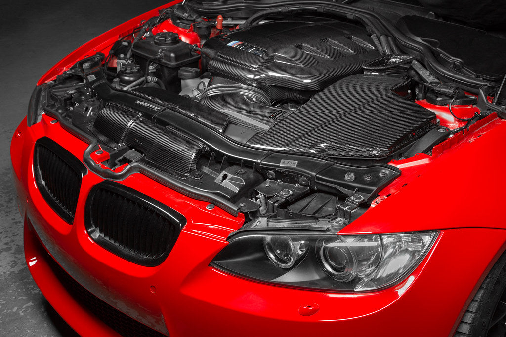 Eventuri gloss carbon fiber duct set installed in the engine bay of a red BMW E92 M3 Coupe