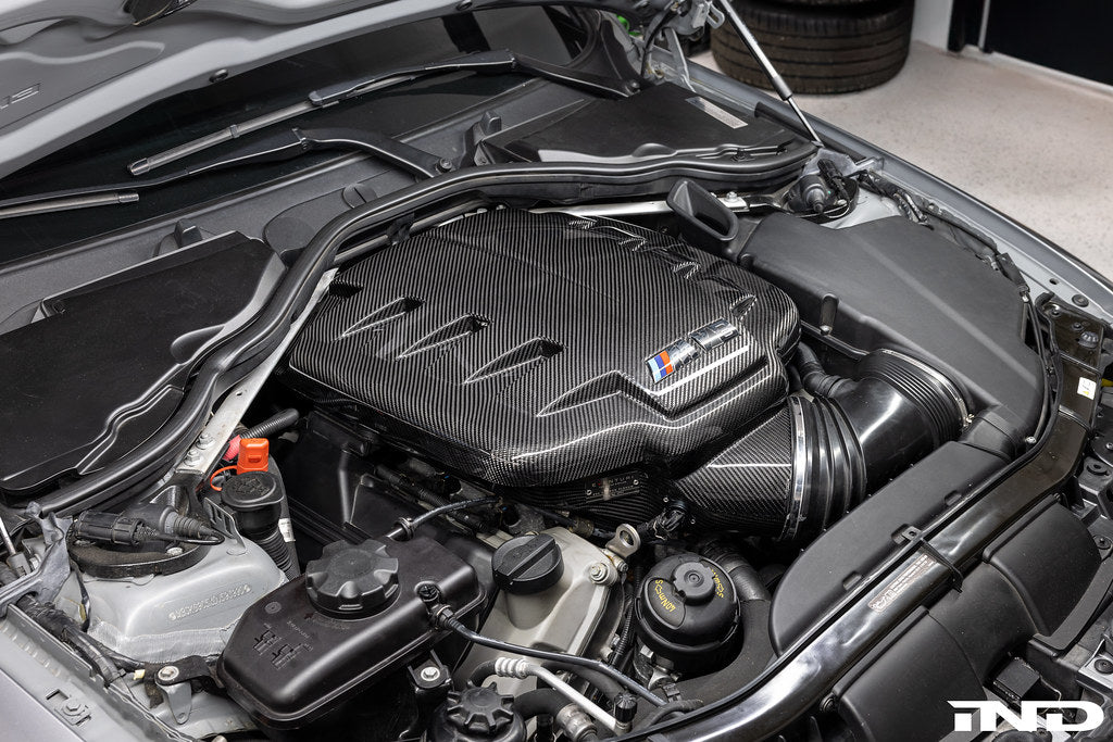 Eventuri black carbon inlet plenum installed in BMW E9X M3 S65 engine bay, showcasing glossy performance intake component.