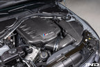 Eventuri black carbon inlet plenum installed in BMW E9X M3 engine bay, showcasing glossy performance carbon fiber for enhanced airflow.