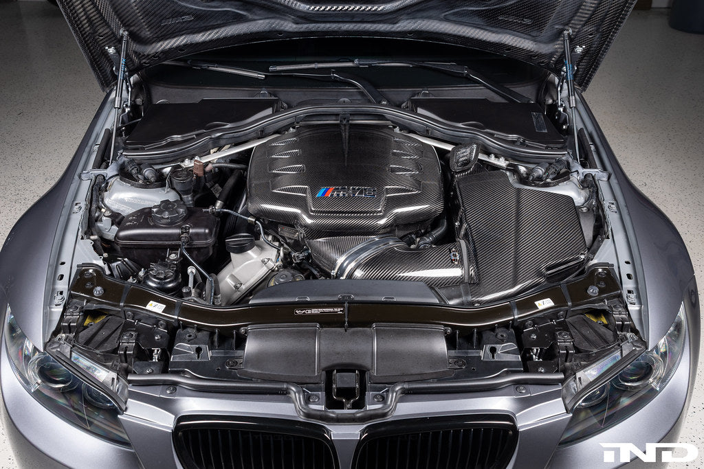 Eventuri black carbon inlet plenum installed in engine bay on BMW E9X M3 S65, showcasing glossy performance upgrade.