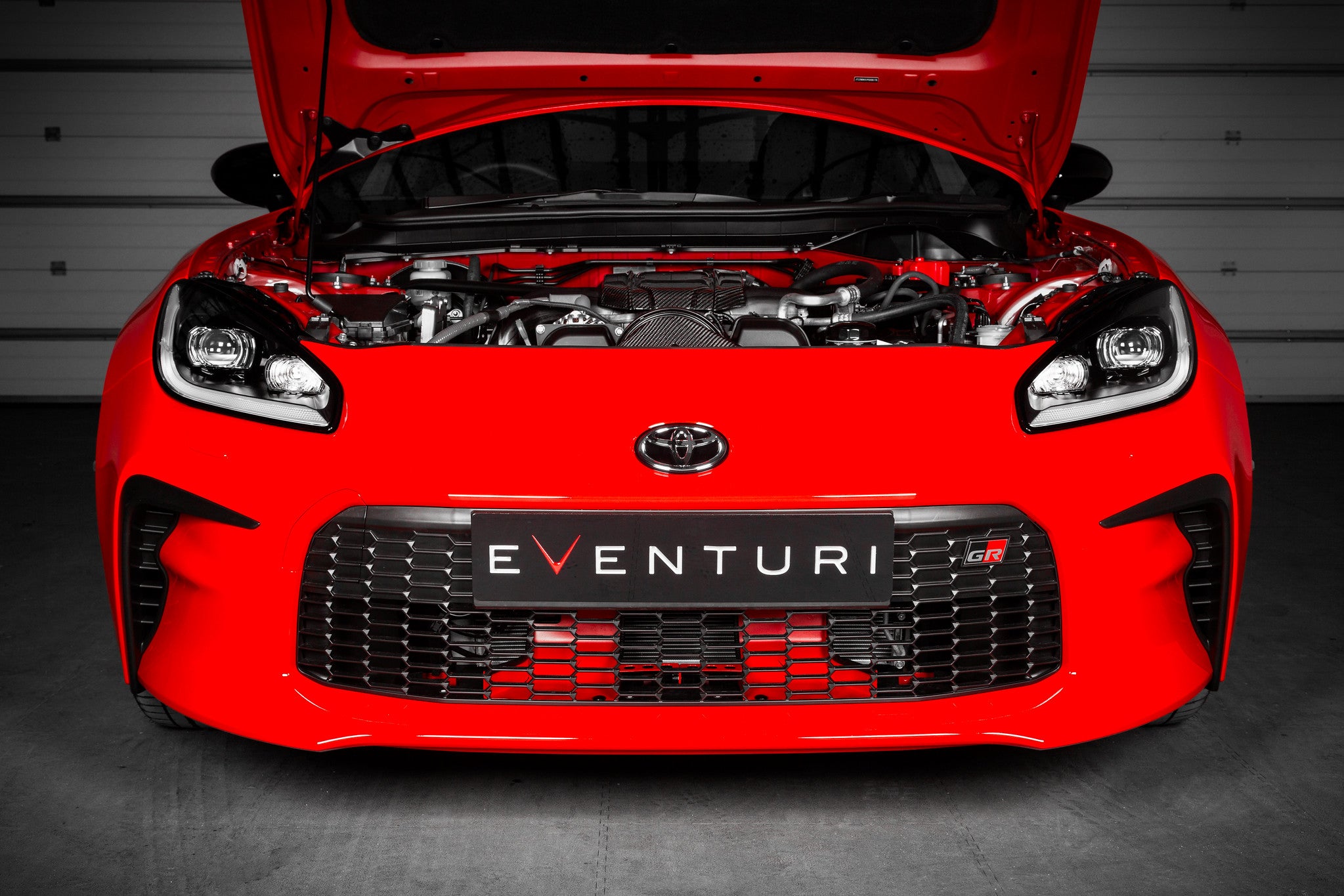 Eventuri Toyota GR86 black carbon intake system installed, showing the performance air intake with engine cover in a car engine bay.