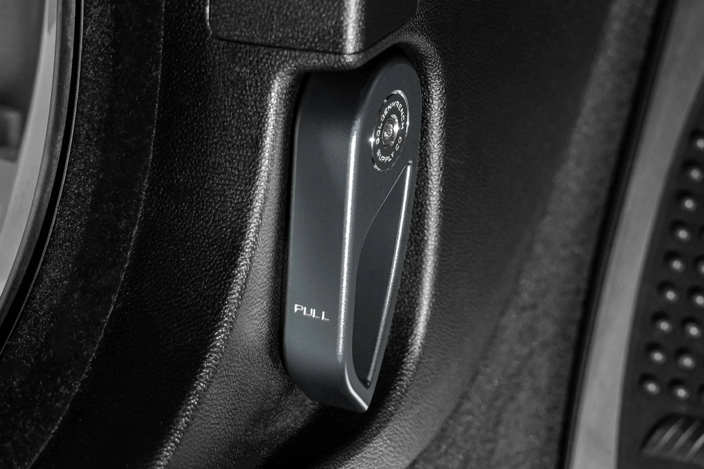 Goldenwrench Blackline Performance BMW M car E-Chassis hood latch handle installed, interior component in anthracite grey.