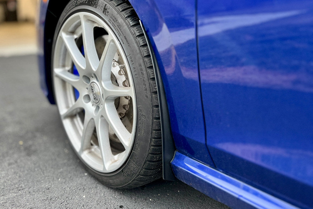 Megachip MK8 GTI and Golf R splash guard set installed on the front of a vehicle, showing exterior protection for wheels and undercarriage.