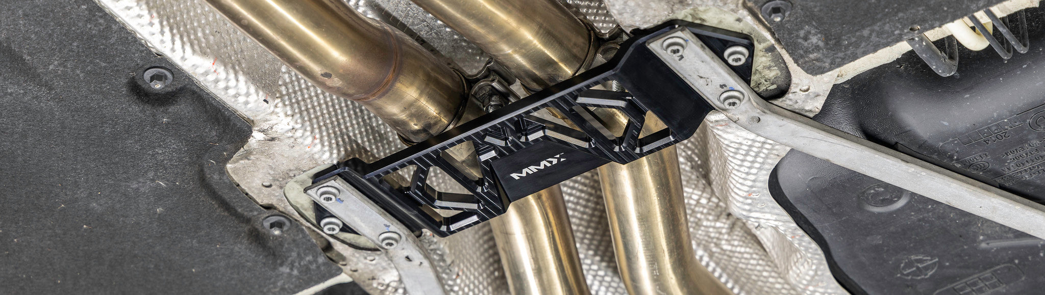 MMX Performance Underbody Chassis Brace installed on a BMW F87 M2, M2 Competition, F80 M3, or F82/F83 M4, providing an additional 15mm of exhaust clearance, improved chassis rigidity, and a direct OEM-fit installation for aftermarket exhaust systems.