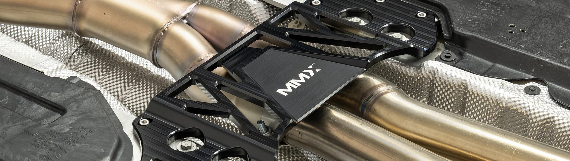MMX Performance billet 6061-T6 aluminum underbody chassis brace installed on a BMW G82 M4, providing an additional 15mm of exhaust clearance while increasing chassis rigidity for improved performance and aftermarket exhaust compatibility.