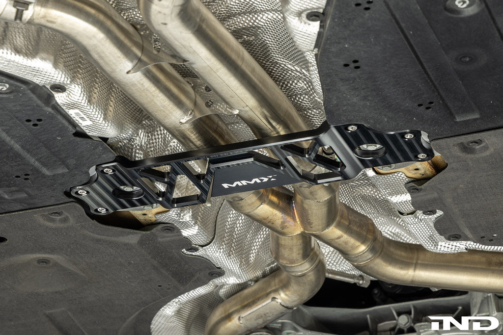 MMX Performance BMW G87 M2 Underbody Chassis Brace installed, providing an additional 15mm of exhaust clearance while maintaining factory ground clearance and increasing chassis rigidity with a precision billet 6061-T6 aluminum design.