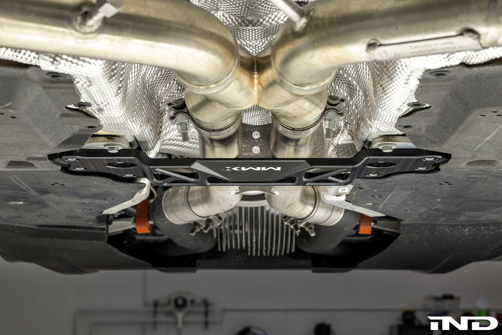 MMX Performance BMW G87 M2 Underbody Chassis Brace installed, providing an additional 15mm of exhaust clearance while maintaining factory ground clearance and increasing chassis rigidity with a precision billet 6061-T6 aluminum design.