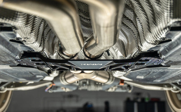 MMX Performance BMW G8X M3 and M4 underbody chassis brace installed, showing the additional 15mm of exhaust clearance beneath the vehicle while maintaining factory ground clearance for improved aftermarket exhaust fitment.